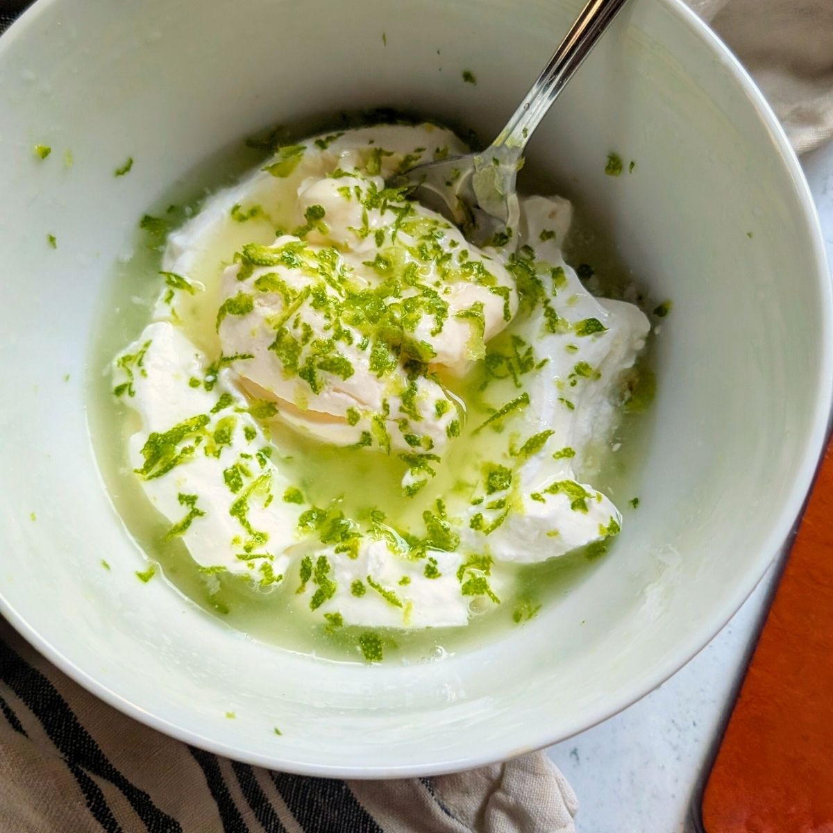 sour cream, mayonnaise, lime juice, and lime zest in a bowl being mixed for street corn.