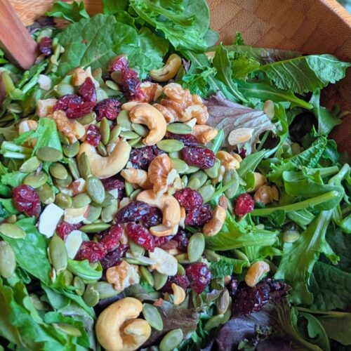 a bowl of salad topper with unsalted nuts and seeds and dried cranberries